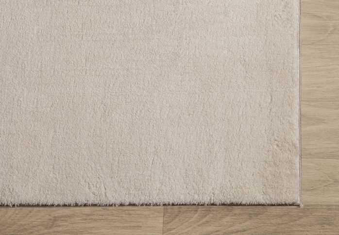 Zoom sur l'angle d'un tapis LOFT beige illustrant la finition soignée des bordures et la densité des poils blancs cassés.