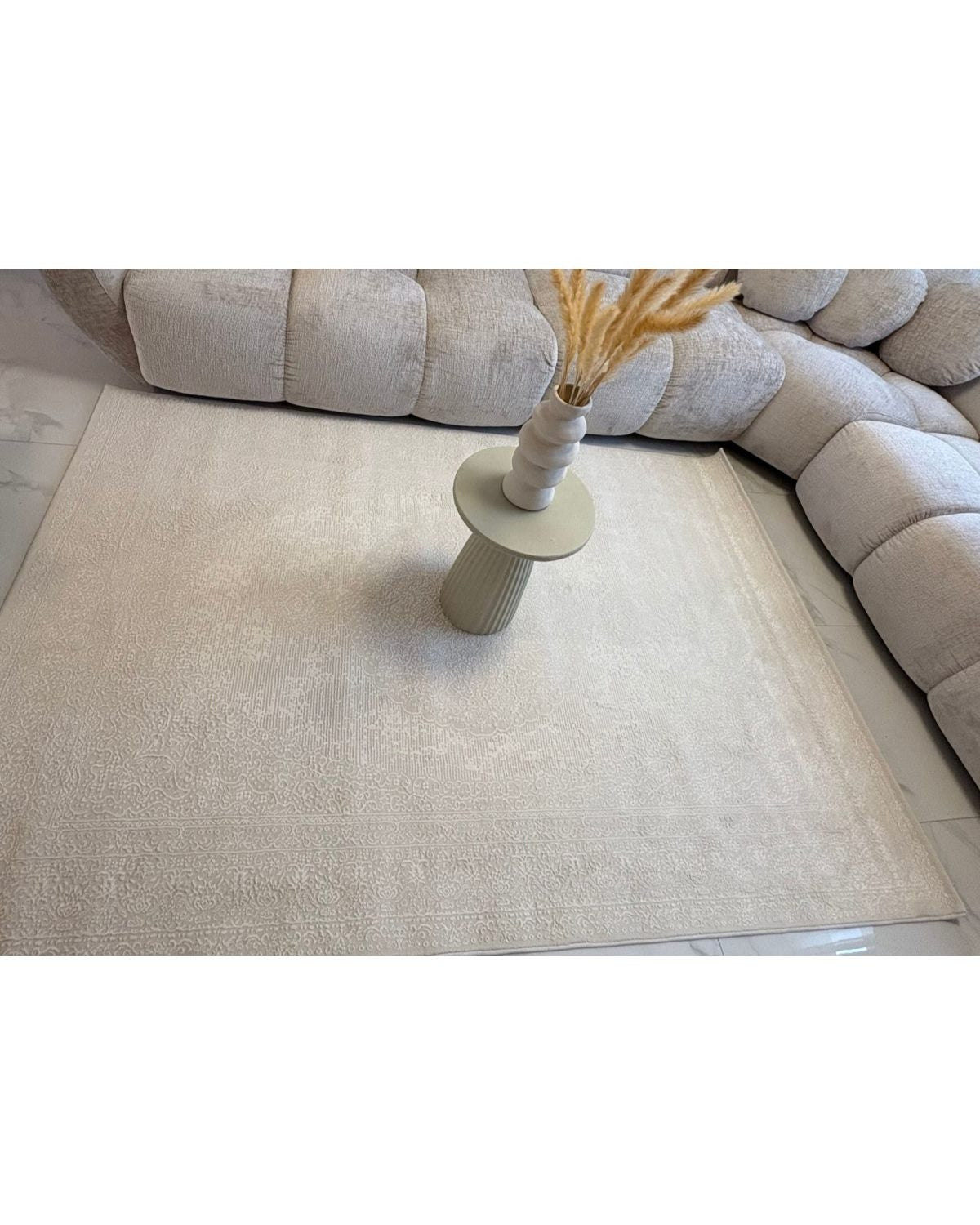 Rendu réel du tapis SIGNO 06 crème chez un client, associé à un canapé design beige et une décoration épurée.