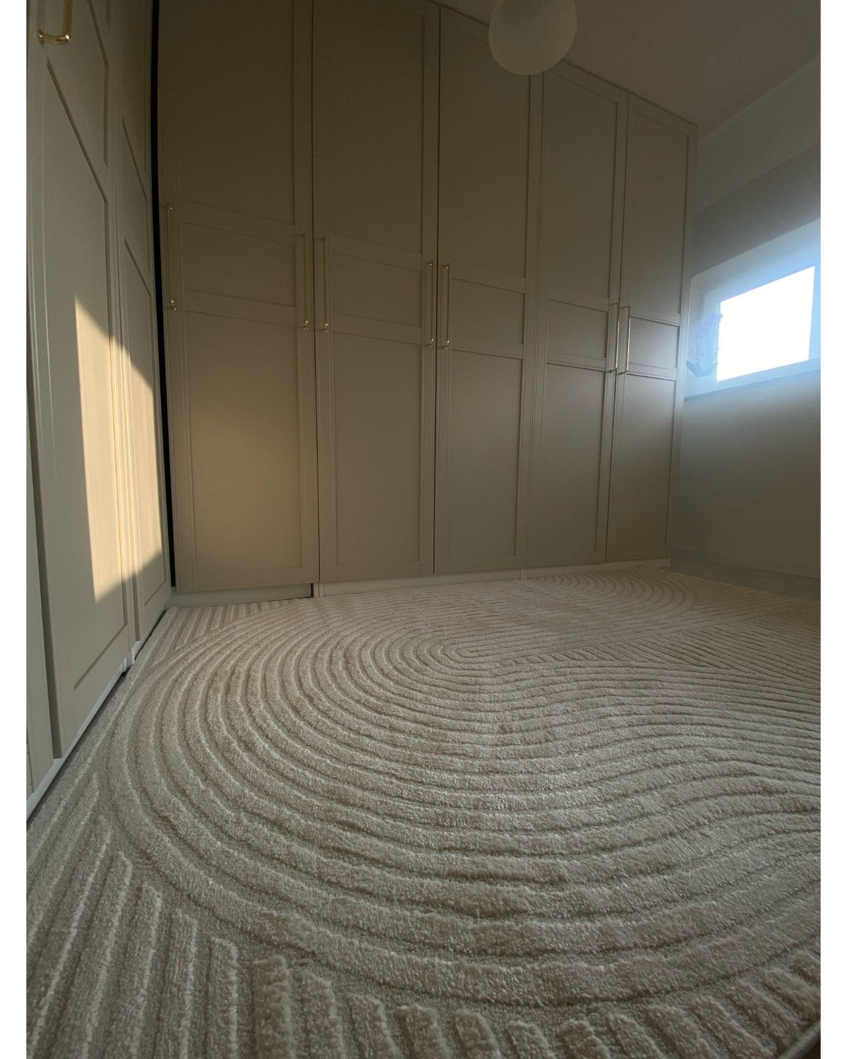 Tapis crème ELIO 51 avec motifs d'arches en relief dans un dressing au style moderne organique et épuré.