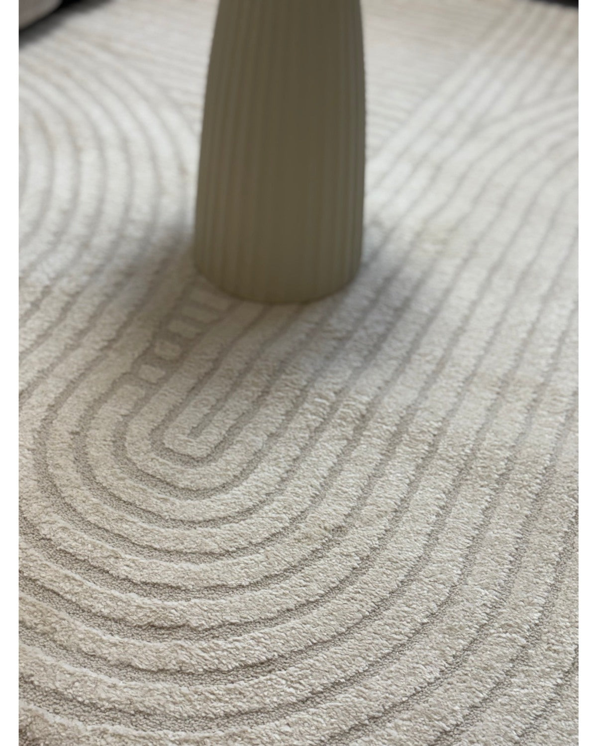 Gros plan sur les motifs en arc de cercle du tapis ELIO 51 crème, montrant le relief sculpté et la densité des fibres.