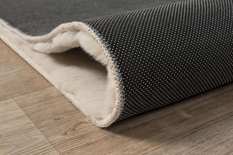 Démonstration de la souplesse du tapis Bubble beige : dossier antidérapant flexible permettant un pliage facile pour le lavage en machine à 30°C.