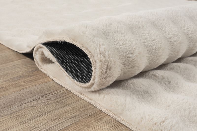 Démonstration de la souplesse du tapis Bubble beige : dossier antidérapant flexible permettant un pliage facile pour le lavage en machine à 30°C.