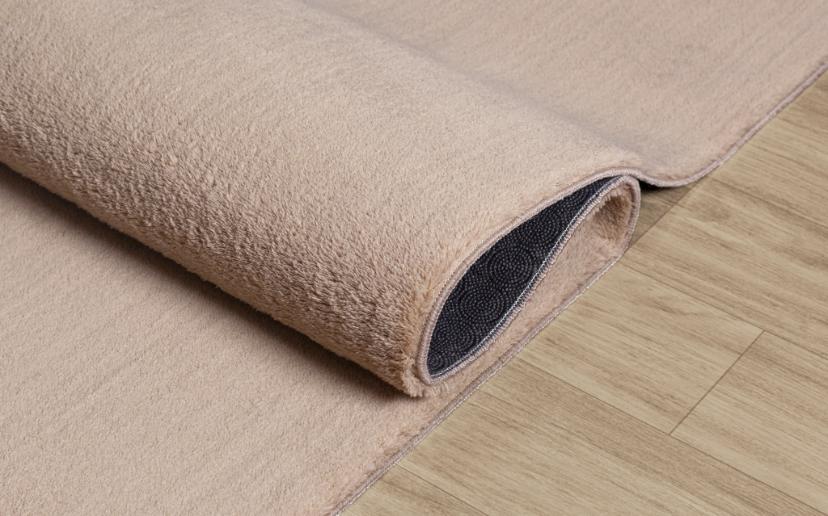 Tapis LOFT beige foncé plié et prêt pour le lavage en machine, démonstration de la souplesse et de la facilité d'entretien.