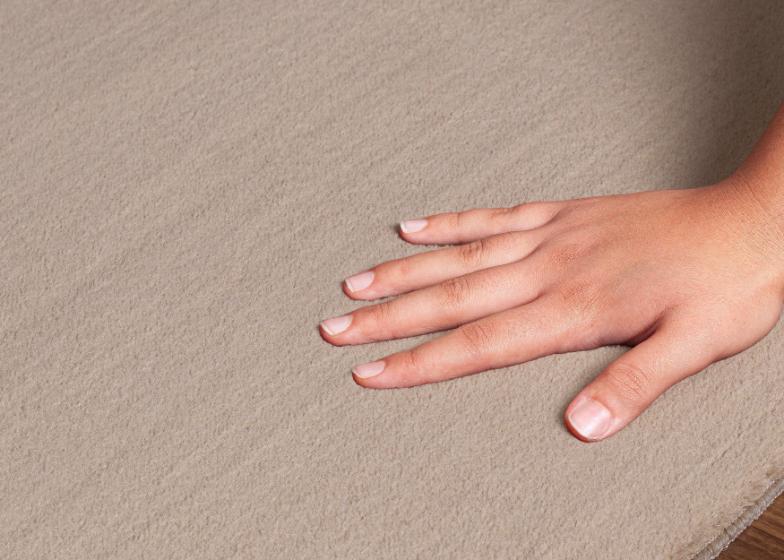 Main plongeant dans les poils hauts du tapis LOFT beige foncé pour montrer l'épaisseur et la douceur extrême de la fibre.