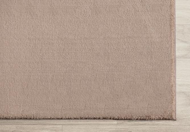 Détail du coin d'un tapis LOFT beige foncé montrant la finition robuste des bordures et la hauteur des poils.