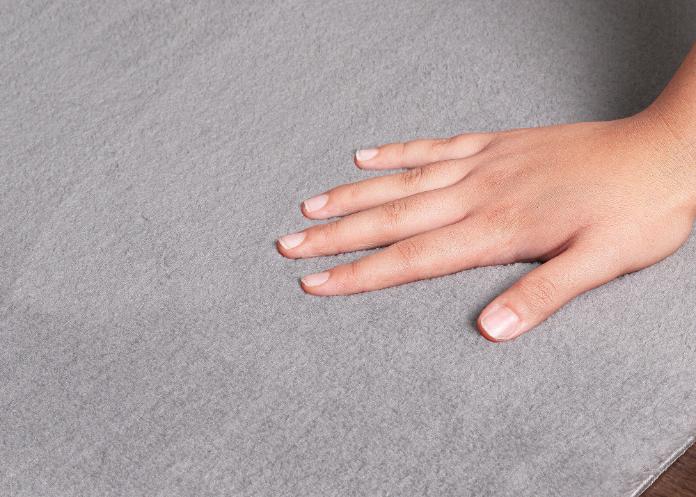 Main plongeant dans l'épaisseur du tapis LOFT gris clair pour illustrer la douceur des fibres et le confort moelleux.