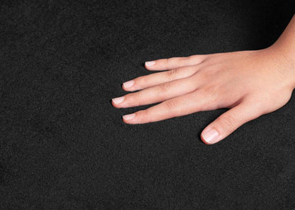 Main caressant la fibre dense du tapis LOFT noir, montrant le contraste entre la peau et le noir profond pour souligner l'épaisseur premium.