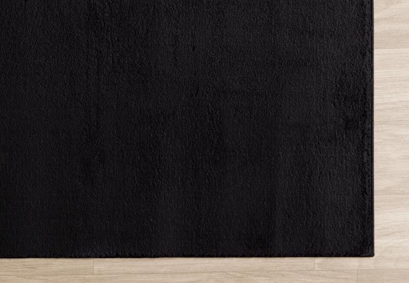 Zoom sur le coin d'un tapis LOFT noir illustrant la qualité des bordures et les reflets soyeux des poils hauts sous la lumière.