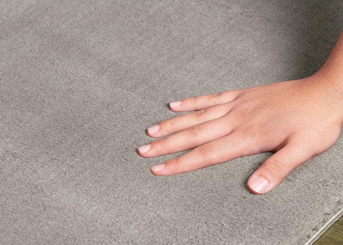 Main plongeant dans l'épaisseur du tapis LOFT taupe pour illustrer la douceur des fibres et le confort moelleux.